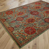 An ornate rectangular area rug with an unusual floral design in green and autumnal colours, shown laid out on a light-coloured wooden plank floor.