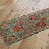 A long runner with a distressed traditional pattern in teal, amber, crimson, and pale gold, shown laid out diagonally on a light wood plank floor.