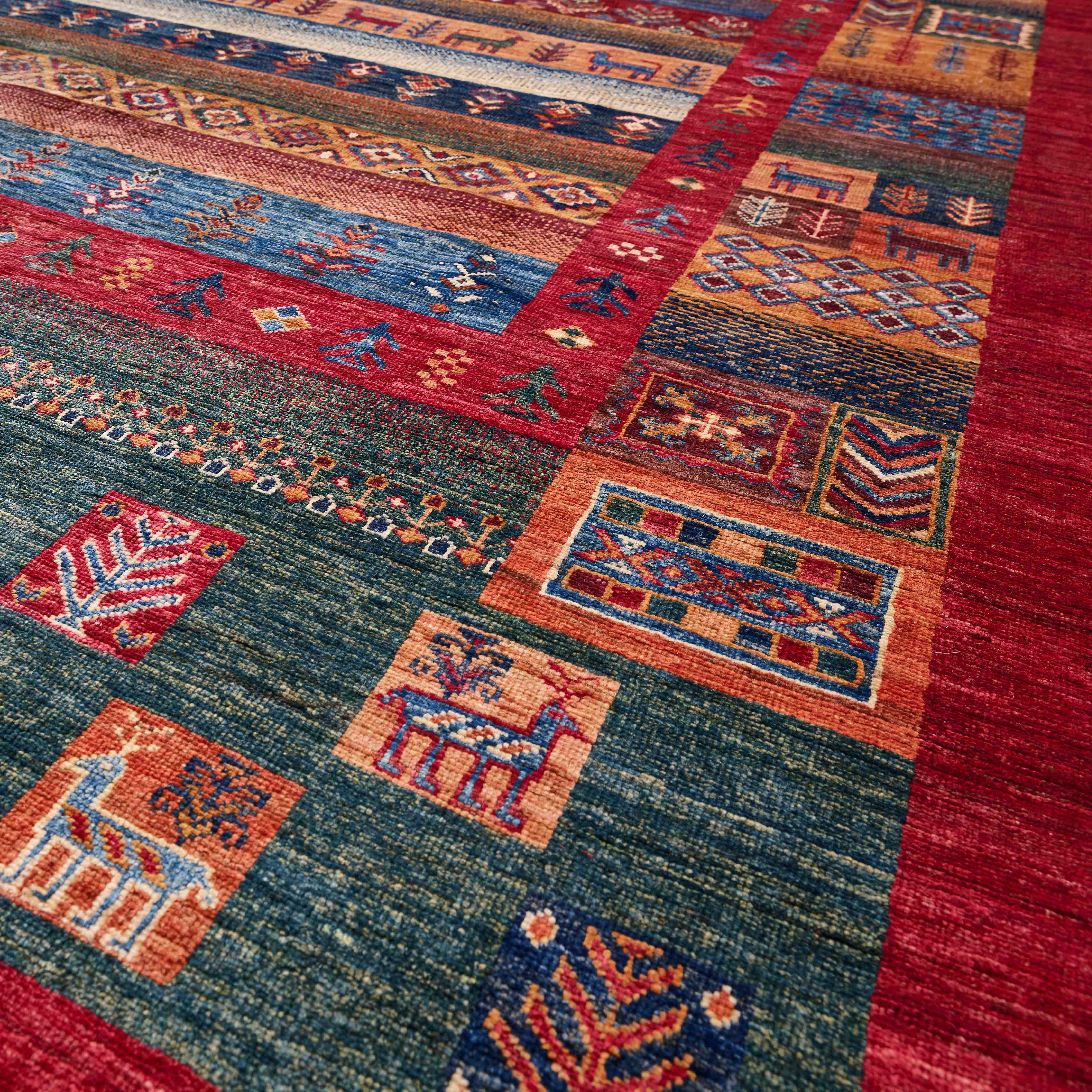 A close-up of a hand-woven Afghan rug with a geometric pattern in red, blue, orange, and green, featuring stylised animal motifs.